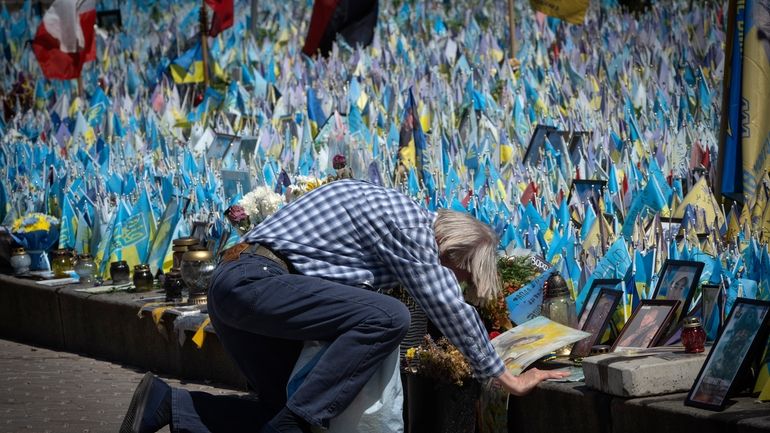 A man kneels in front of a makeshift memorial for...