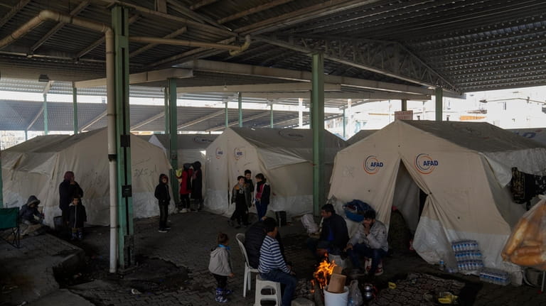 Syrian refugees warm themselves in front of a fire by...