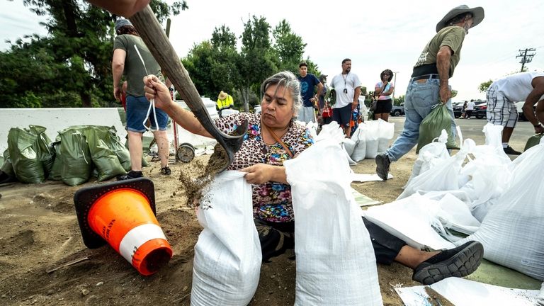 Seated on the ground, Norma Panilla meticulously bags sandbags at...