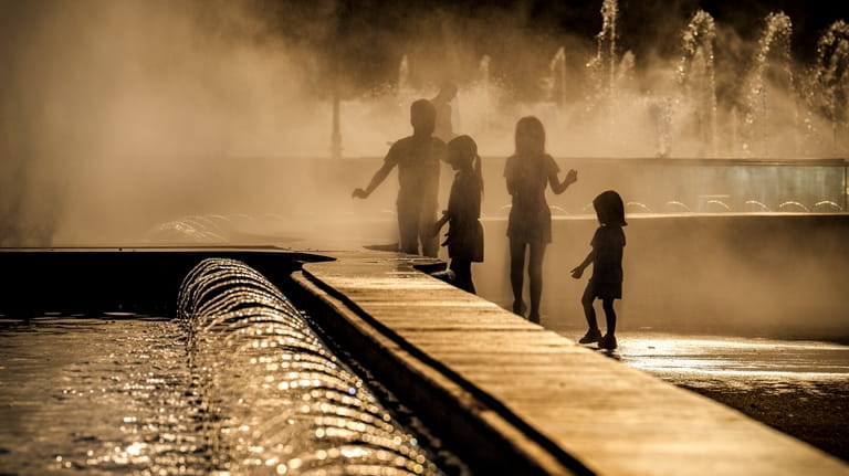 Children enjoy the drizzle from a public fountain before sunset...