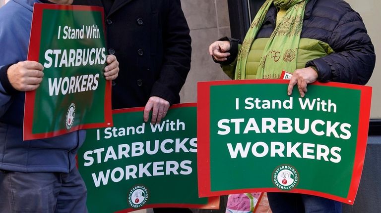 Three people hold signs supporting Starbucks workers gather outside a...