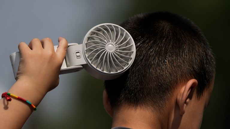 A boy cools himself with an electric fan on a...