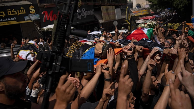 A gunman holds up his weapon as mourners carry the...