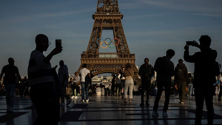People use their smartphones near the Olympic rings that are...