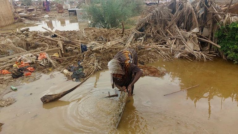 A woman sorts through floodwaters near her damaged home near...