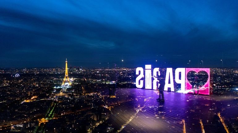 A visitor strolls past a "Paris" sign that is reflected...