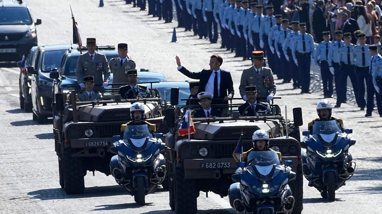 French President Emmanuel Macron waves from the command car as...