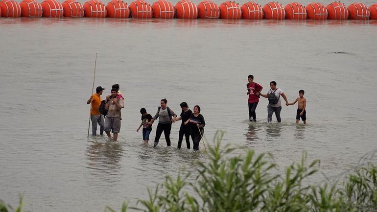 Migrants who crossed the Rio Grande from Mexico walk past...