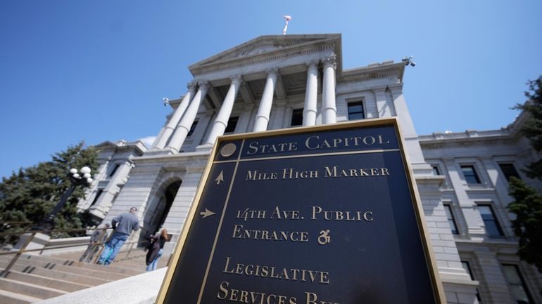 Visitors stand on the west steps of the Colorado Capitol,...