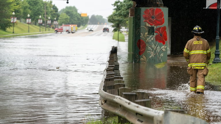 A firefighter walks past a flooded Saginaw Rd. as rains...
