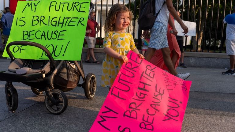 Louisa Monje, 2, from Washington, holds a sign in front...