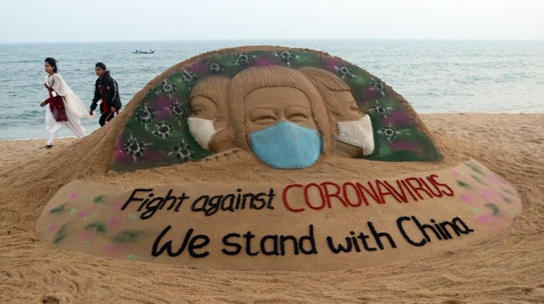 People walk Monday near a sand sculpture at Puri beach...