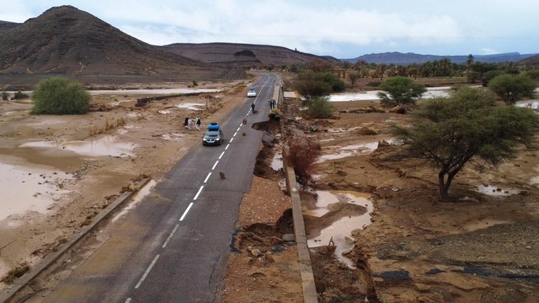 Cars drive through a road that was damaged by floods...