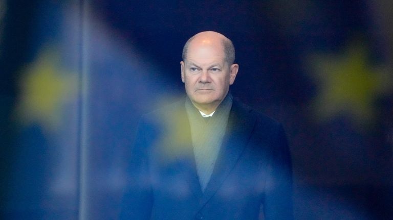 German Chancellor Olaf Scholz stands behind a reflection of the...