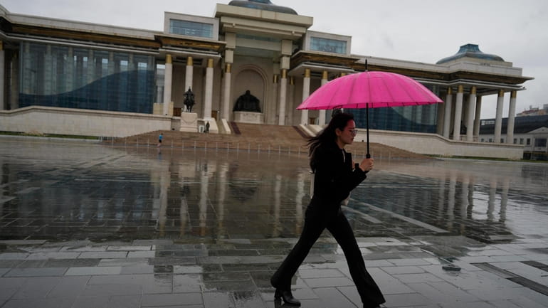 A woman walks carrying an umbrella as it rains on...