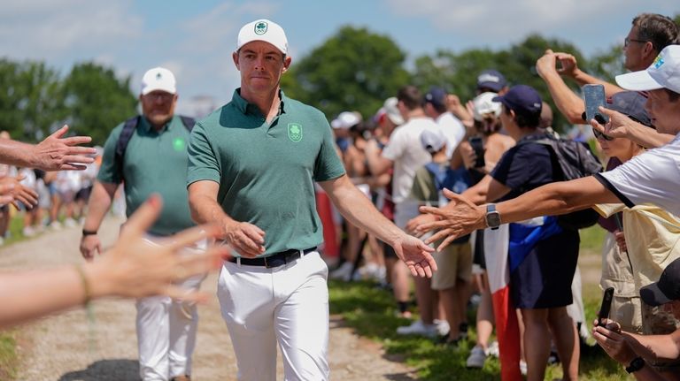 Rory McIlroy, of Ireland, taps hands with fans as he...