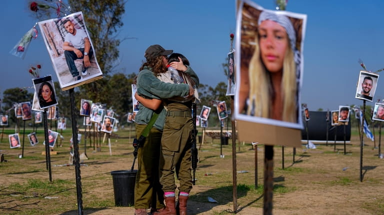 Israeli soldiers embrace next to photos of people killed and...