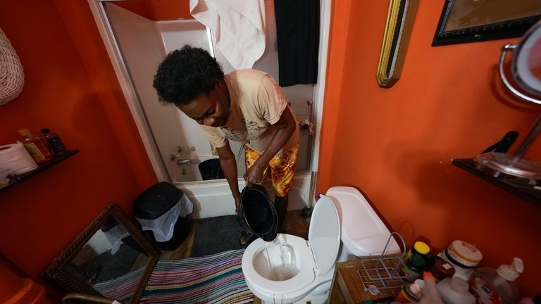 Leonard Kately pours water from a bucket to flush the...