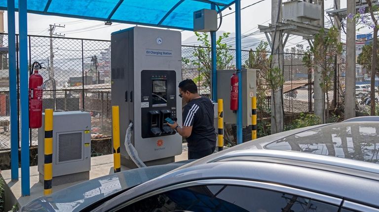 A man charges his electric vehicle at a charging station...