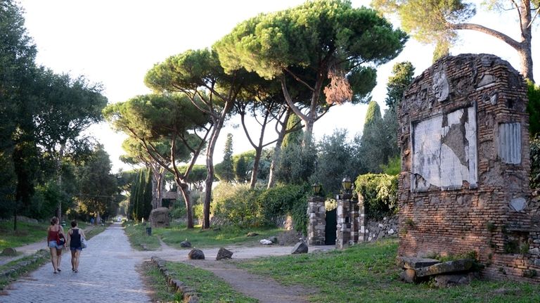 People walk past ruins along the Appia Antica, the ancient...