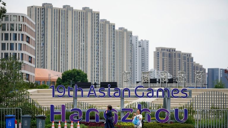 People walk past by signboard of the 19th Asian Games...