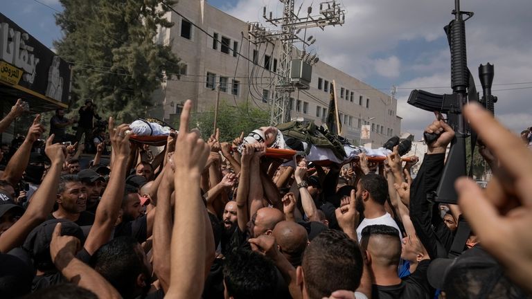 Mourners, some armed, carry the bodies of Palestinian men who...