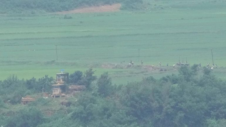 North Koreans work on a field near a North Korean...