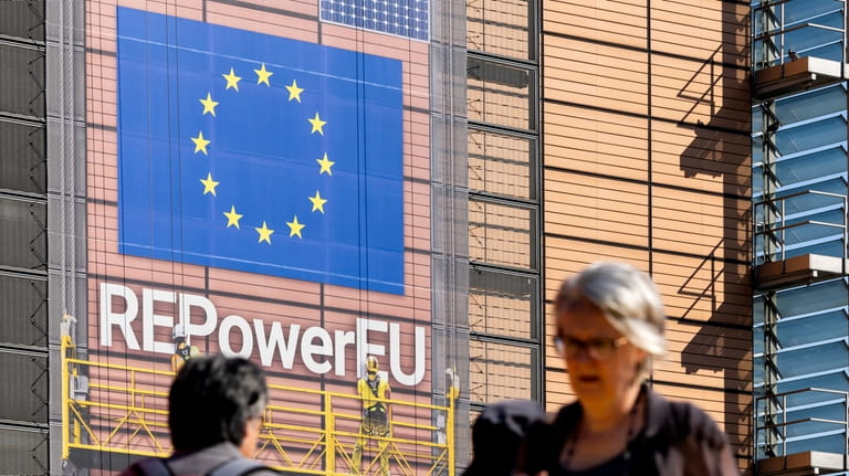 Pedestrians walk in front of a banner outside EU headquarters...