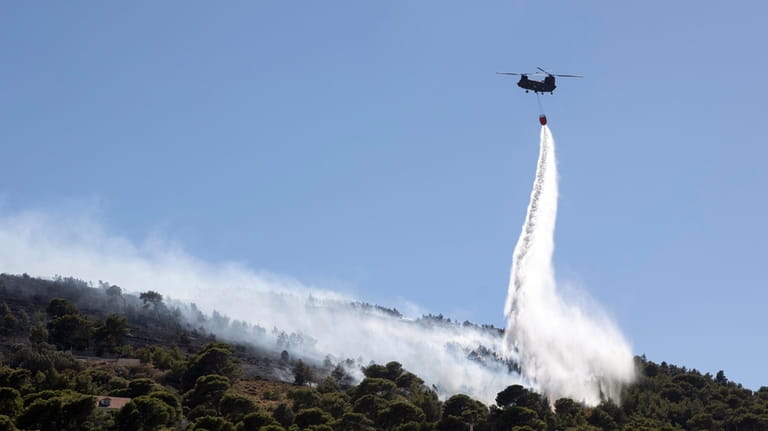 A firefighting helicopter throws water over a wildfire at Keratea...