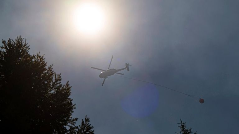 A helicopter carries waters over the Park Fire near Forest...