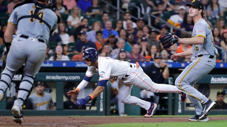 Houston Astros' Jeremy Pena, center, dives for home plate between...