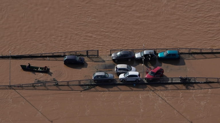 Cars sit on a submerged road in an area flooded...