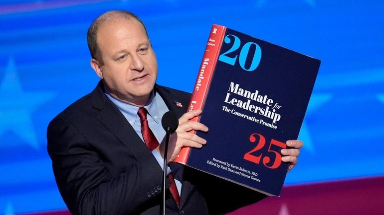 Colorado Gov. Jared Polis holds up a copy of Project...