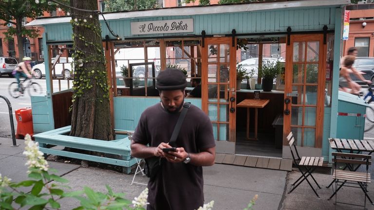 A pedestrian stops on the sidewalk beside the outdoor dining...