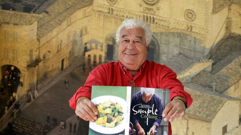 Italian chef Antonio Carluccio holds a copy of his cookbook...