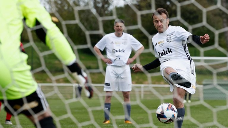 French President Emmanuel Macron scores a penalty as he participates...