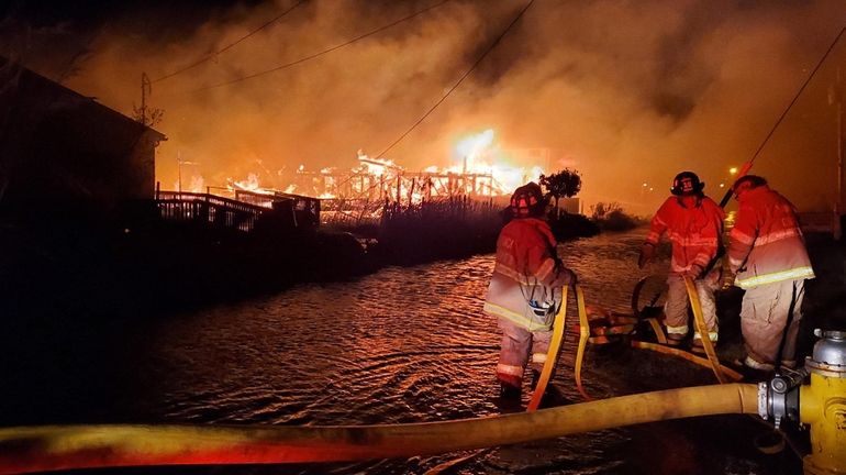 Firefighters battle a windswept blaze that destroyed three homes in...