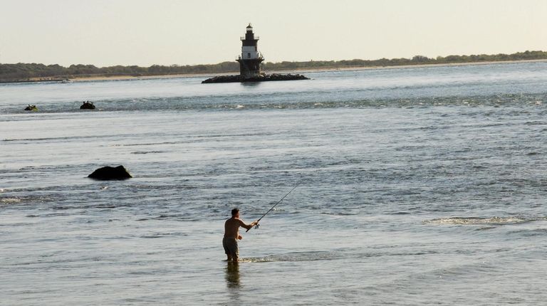 A man fishes off a sandbar with Orient Point Light...