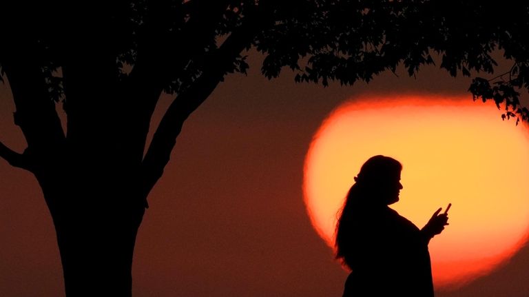 A woman looks at her phone while watching the sun...