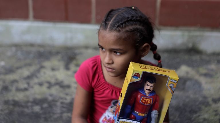 A child holds a "Super Bigote" action figure doll modeled...