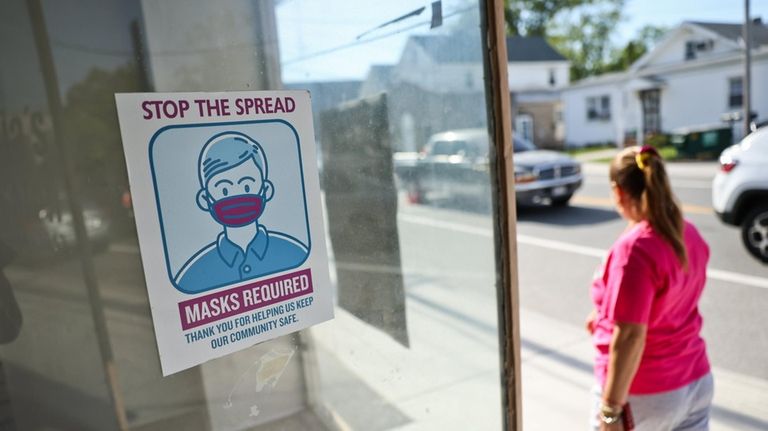 A person passes a storefront with a posted mask sign...