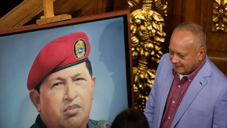 Lawmaker Diosdado Cabello stands next to an image of late...