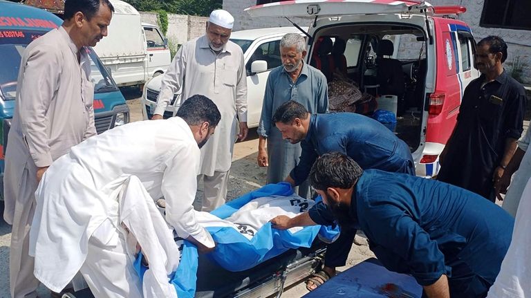 Volunteers and relatives prepare to load the body of a...