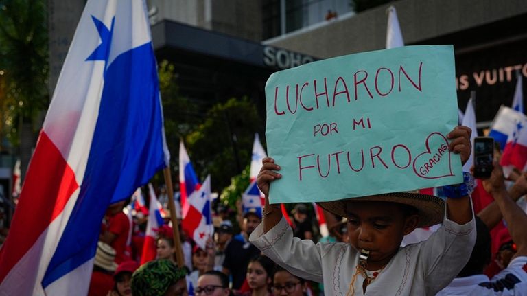 A boy holds a sign that reads in Spanish “They...