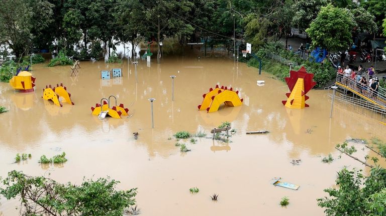 People look on a submerged dragon structure in a playground,...