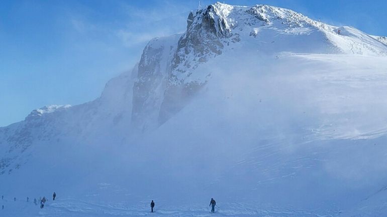 Skiers take off from the top of a mountain at...