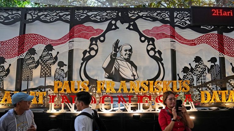 People walk past a welcoming signboard for Pope Francis displayed...