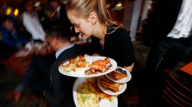 A waitress carries breakfast dishes to customers at a restaurant...