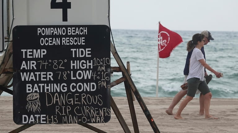 Beachgoers walk past warning flags and signs, Jan. 13, 2020,...