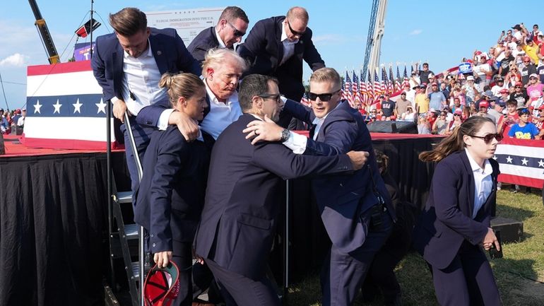 Former President Donald Trump is helped offstage after a shooting...